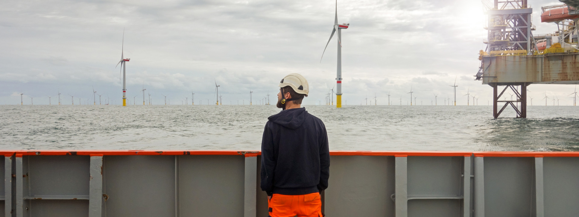 Man with hard hat looking out towards a wind turbine